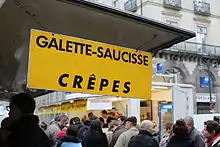 Photographie présentant l'écriteau d'un stand de vente, et une foule de personnes.