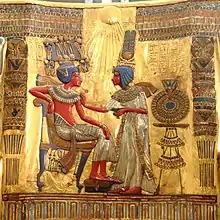 Toutânkhamon, à gauche, est assis sur son trône. Son épouse est debout face à lui, sur la droite de l'image.