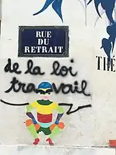 Graffiti "Rue du Retrait de la loi Travail" détournant la plaque indiquant la rue du Retrait, sur un mur parisien.