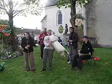 photo couleur d'un groupe musical en plein air devant une église. Les instruments sont une cabrette, une clarinette, un graïle et des percussions.