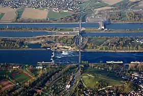 Le Rhin (au 1er plan), puis le canal séparé en deux avec une écluse et, au fond, une centrale hydroélectrique.