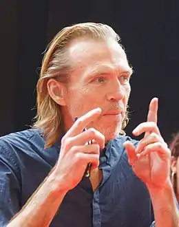 Homme aux cheveux longs et blonds portant une chemise bleue.