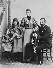 Photographie en noir et blanc montrant une femme debout entourée de deux petites filles (à gauche) et d'un homme assis tenant un petit garçon sur ses genoux (à droite).