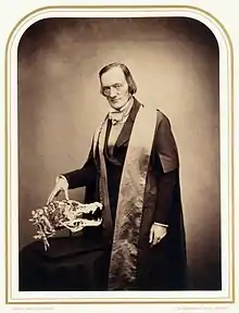 Photographie d'un homme de trois quarts, une main posée sur un crâne.