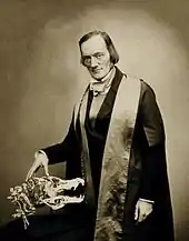 Richard Owen, posant debout à côté d'un crâne de crocodile sur laquelle il pose la main.
