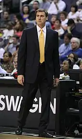 Portait de Rick Carlisle en costume noir et cravate jaune dirigeant son équipe du bord du terrain