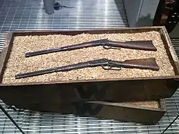 Photo représentant des caisses en bois dont une est ouverte et contient des fusils.