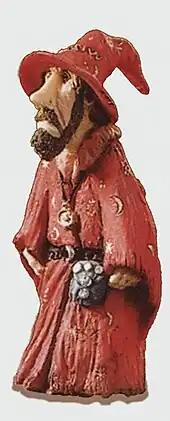 Une figurine d'un homme au visage triste, avec une barbe courte, une robe et un chapeau de sorcier rouges.