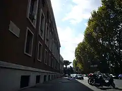 Photographie en couleurs d'une rue dominée par un haut bâtiment en briques.