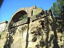 Photographie en couleurs d'un mur de gros blocs maçonnés surmonté d'une arche en pierre.