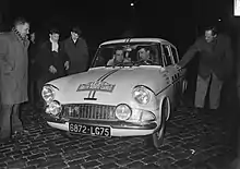 Photographie en noir et blanc montrant deux hommes dans une voiture de course.