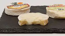 Photo couleur de petits fromages ronds et plats. Celui au premier plan est coupé et laisse voir une pâte molle et coulante couleur crème.