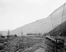 un chemin de fer traversant un village avec un champ de débris rocheux à l'arrière