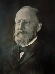 portrait photographique, en noir et blanc, d'un homme d'une soixantaine d'années, au front dégarni, portant un binocle et une barbe claire.