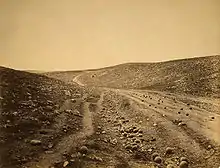 Photographie d'un sentier au milieu d'un paysage rocailleux et vallonné. Des dizaines de boulets sont visibles sur le chemin et dans les fossés alentours.