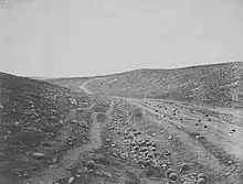 Photographie d'un sentier au milieu d'un paysage rocailleux et vallonné. Des dizaines de boulets sont visibles sur le chemin et dans les fossés alentours.