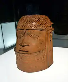 forme cylindrique en laiton représentant un visage humain avec une coiffe tressée