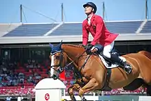 un cavalier en veste rouge sur un cheval à la robe marron durant une compétition de saut d'obstacles