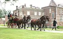 Vue d'un attelage à quatre chevaux bais devant une très belle demeure en pierre ; les passagers sont habillés élégamment.