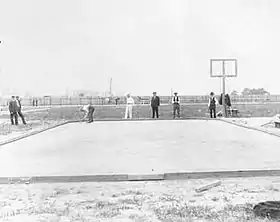 Photographie en noir et blanc d'un terrain couvert de sable entourés par des sportifs et des juges