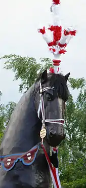 Tête d'un grand cheval de bois de couleur brun foncé, surmontée d'un plumeau rouge et blanc.