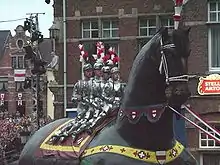 Photographie d'un cortège de carnaval montrant un géant du Nord : le géant est un cheval et quatre adolescents en armures, épées levées, sont juchés sur cette figure de cortège