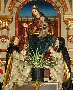 Statue de la Vierge Marie tenant l'enfant Jésus avec un moine et une religieuse agenouillés à ses pieds.