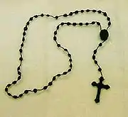 Chapelet catholique avec petites grains et croix latine, noir sur fond crème.
