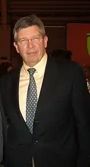 Photo de Ross Brawn en costume, souriant, debout, portant des lunettes