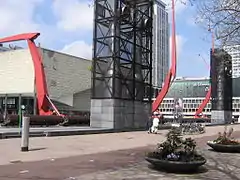 Les grandes lampadaires et les tuyaux verticaux de ventilation sur la place du Théâtre, avec en arrière-plan la tour Millenium et De Doelen.