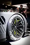 Photo de la roue d'une voiture de course grise et noire sur un stand d'exposition.