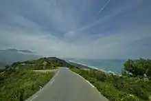 Photo couleur d'une route de bord de mer, sous un ciel bleu nuageux.