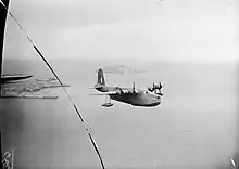 Photo en noir et blanc d'un hydravion quadrimoteur survolant des îles.