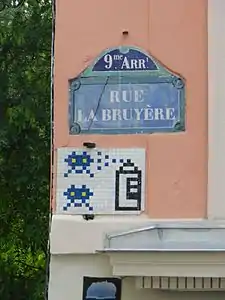 Mosaïque d'Invader sous une plaque de la rue.