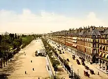 Carte postale en couleur montrant de gauche à droite, un parc, une rue et des immeubles.