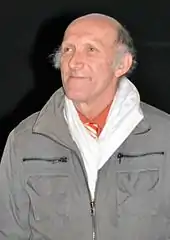 Homme au crâne dégarni et souriant portant un manteau.