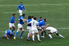 Photographie d'un regroupement dans un match de rugby à XV, entre l'équipe d'Italie en maillots bleus et l'équipe de France en maillots blancs