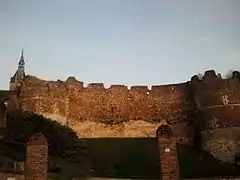 Photo de ruines de teinte orange d'un rempart reliant deux tours d'un ancien château médiéval.