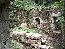 Photo montrant à l'intérieur d'une ruine sans toit deux grosses meules de pierre par terre.