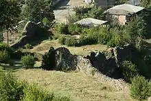 Photo en couleur montrant au premier plan un champ délimité par des murs de pierre et au fond des maisons