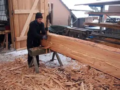 Équarrissage d'un madrier utilisant la doloire de charpentier.