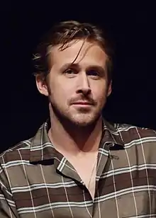Ryan Gosling de face, avec une mèche qui lui traversant le front et une chemise brune.