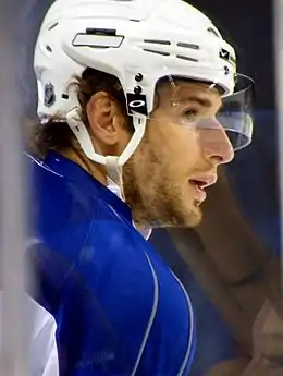 photographie en couleur d'un joueur de hockey avec un maillot bleu et un casque blanc.