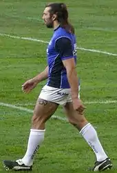 Photo en pied d'un joueur en maillot bleu et short blanc marchant sur le terrain