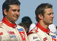 Bustes de Sébastien Loeb et de son copilote Daniel Elena vus de profil en posture solennelle et combinaison automobile.