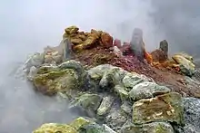 Photographie couleur de fumerolles opaques dans un décor de pierres colorées.