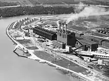 Vue aérienne d'une usine avec trois cheminées au bord d'une rivière.
