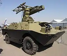 Un véhicule blindé à roues vu de trois-quart, avec un système lance-missiles sur le toit.