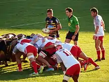 Une mêlée entre joueurs de rugby, avant l'introduction du ballon, sous le regard de l'arbitre et des demis de mêlée.
