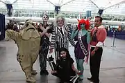 Groupe de six personnes portant des costumes. Celui de droite est une personnification d'Ed Wood, avec une petite moustache et un pull rose porté par-dessus un costume.